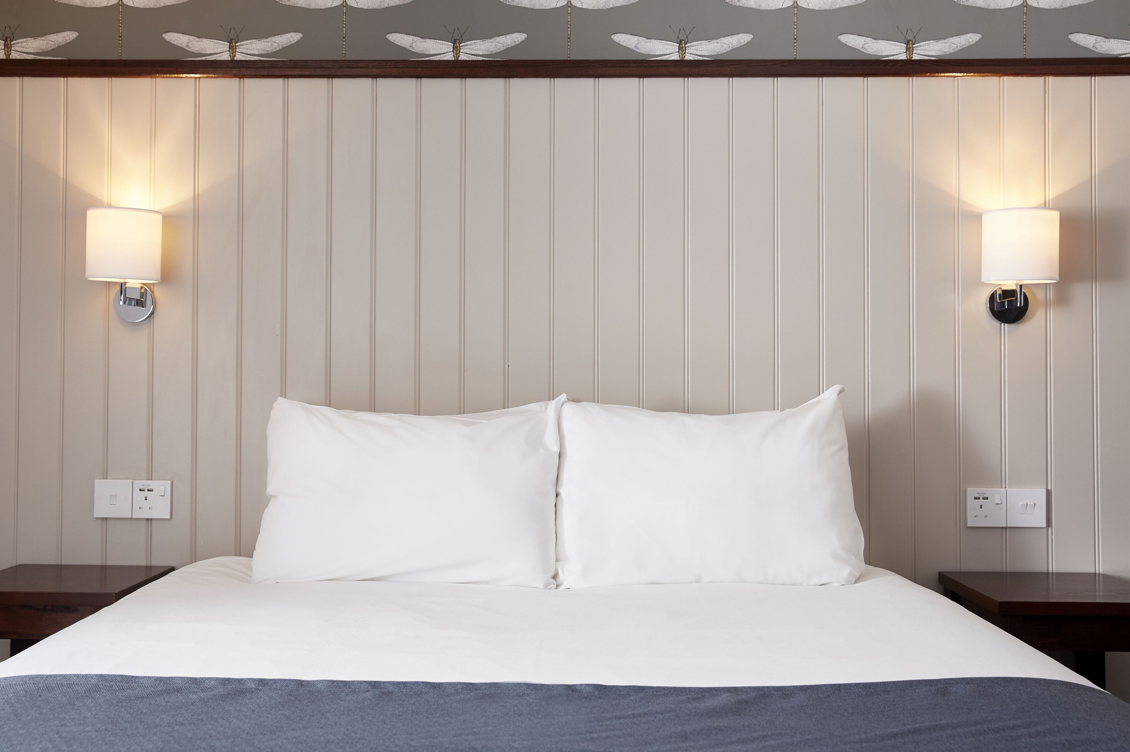 Una habitación de hotel con una cama grande, dos mesitas de noche y lámparas de pared.