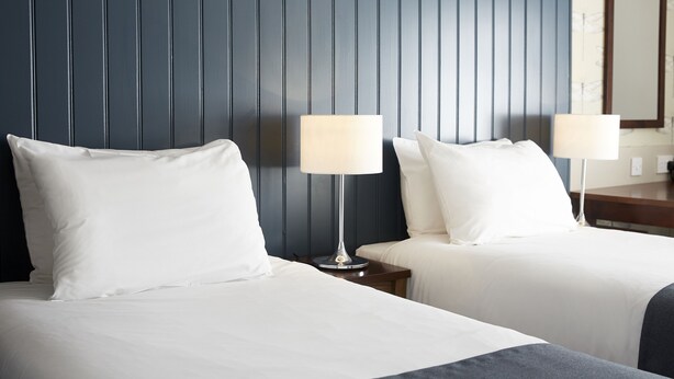Habitación de hotel con dos camas, cada una con ropa blanca y una lámpara a juego.