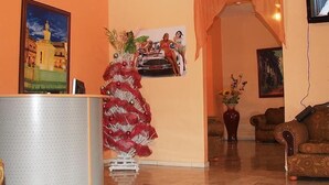 A lobby with a reception desk, a decorative red tree, and a painting of a car. - Hotel Navarro (Santo Domingo)