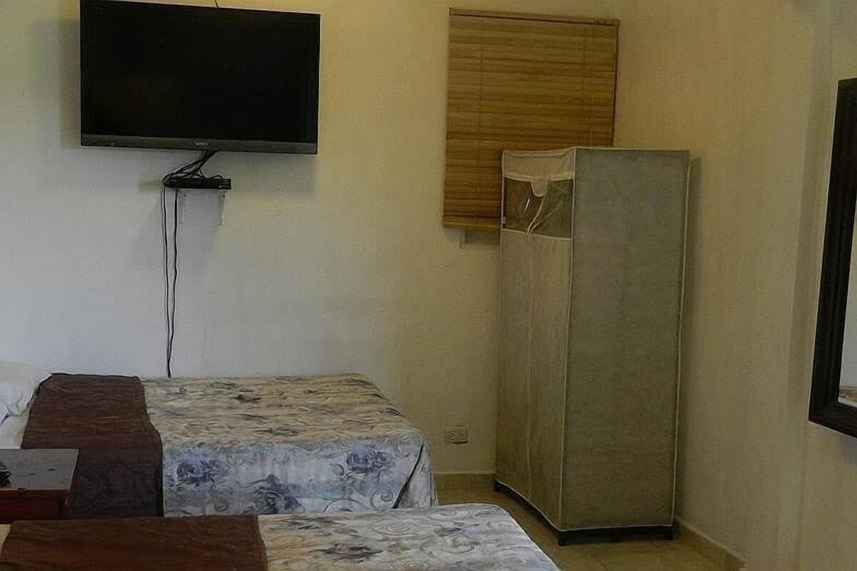 Una habitación pequeña con dos camas, un televisor montado en la pared y un armario.