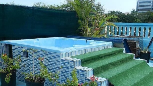 A rooftop swimming pool with a blue tiled exterior, surrounded by potted plants and a staircase leading to a green artificial turf area. - Hotel Navarro (Santo Domingo)