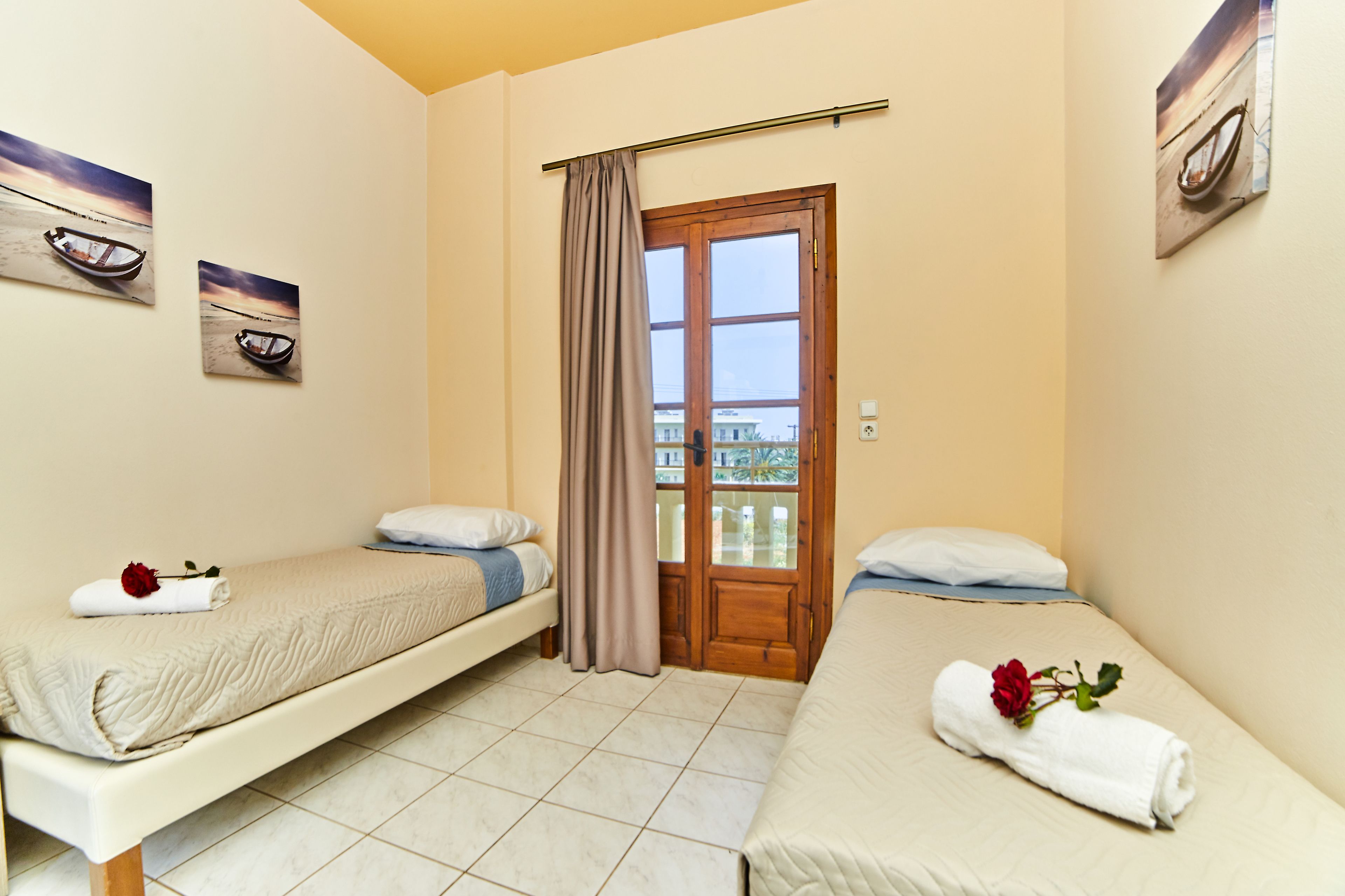 A room with two single beds, a window with curtains, and two paintings on the walls.