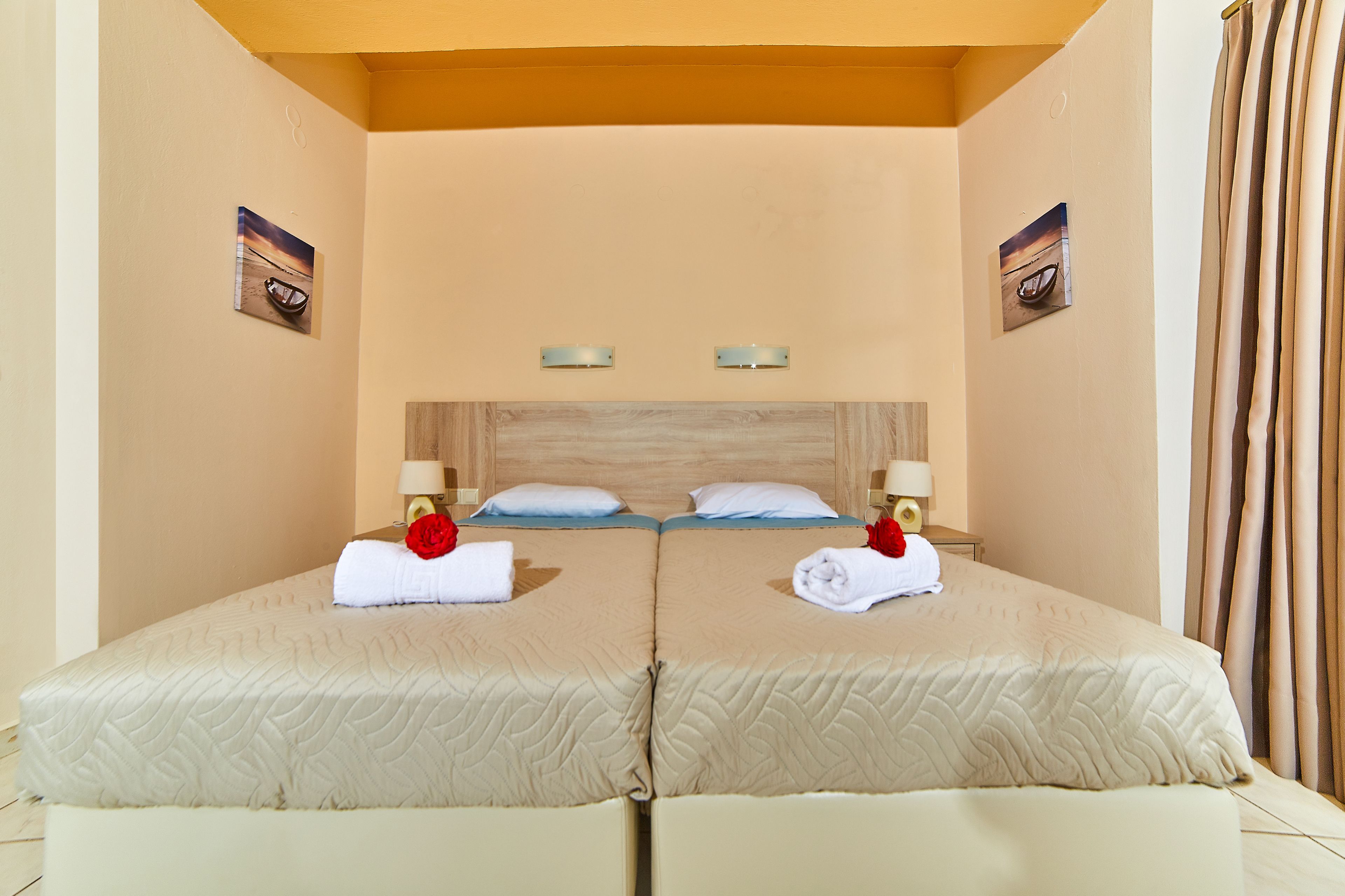 A double room with two beds, each with a headboard, bedside tables, lamps, and artwork on the walls.