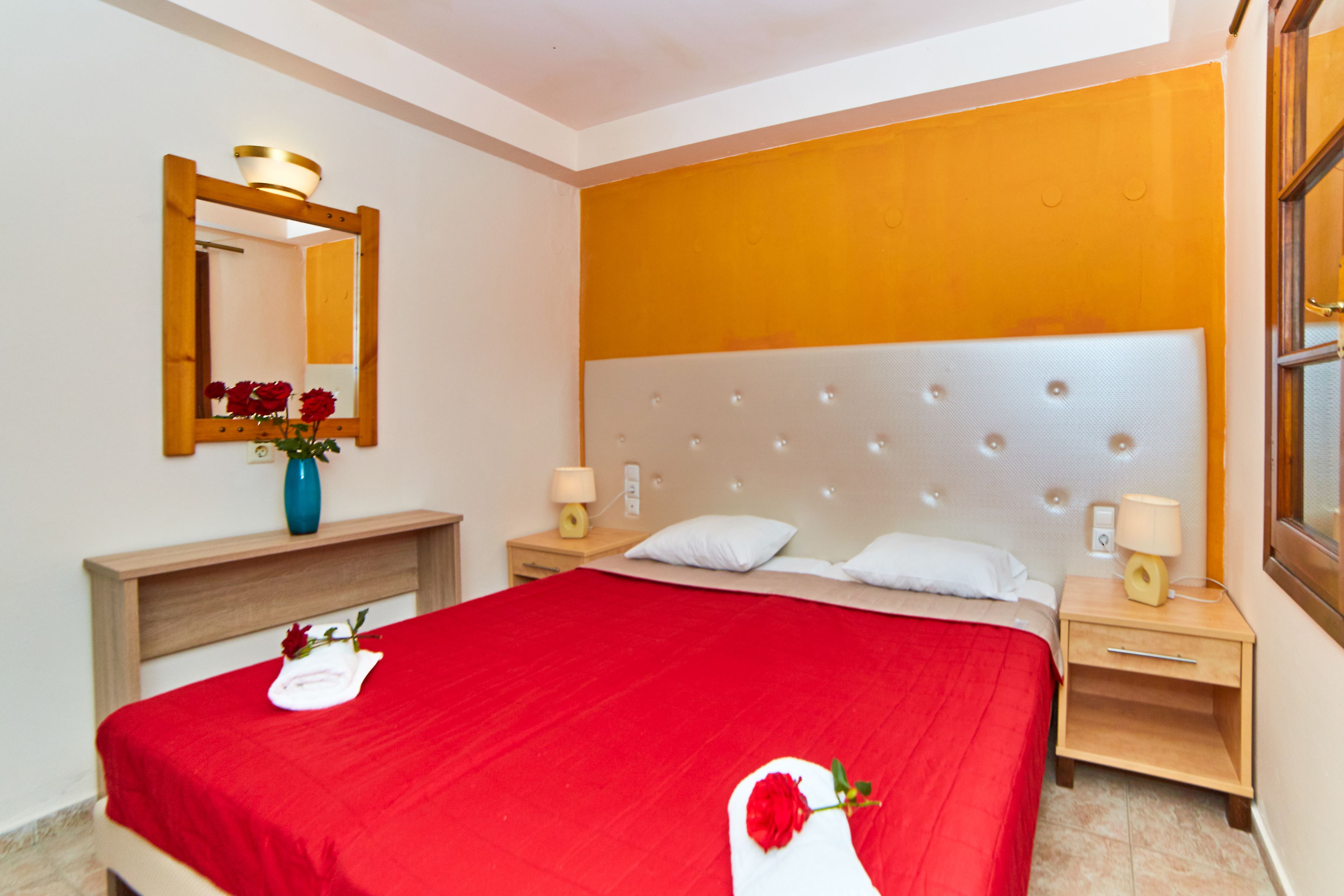 A hotel room with a large bed, wooden headboard, two bedside tables with lamps, a mirror, and a vase with flowers.