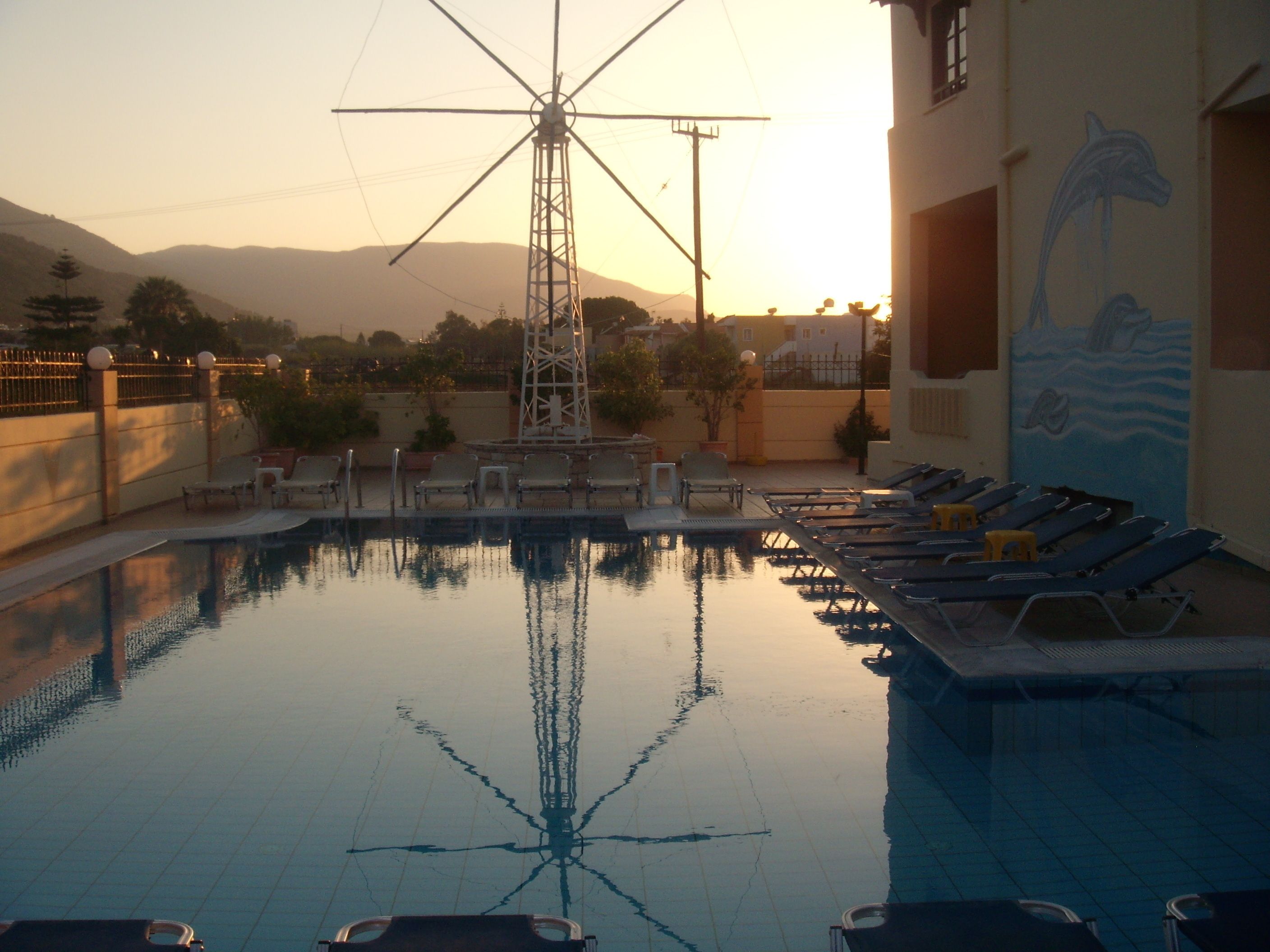 A swimming pool with lounge chairs and a wind turbine in the background.