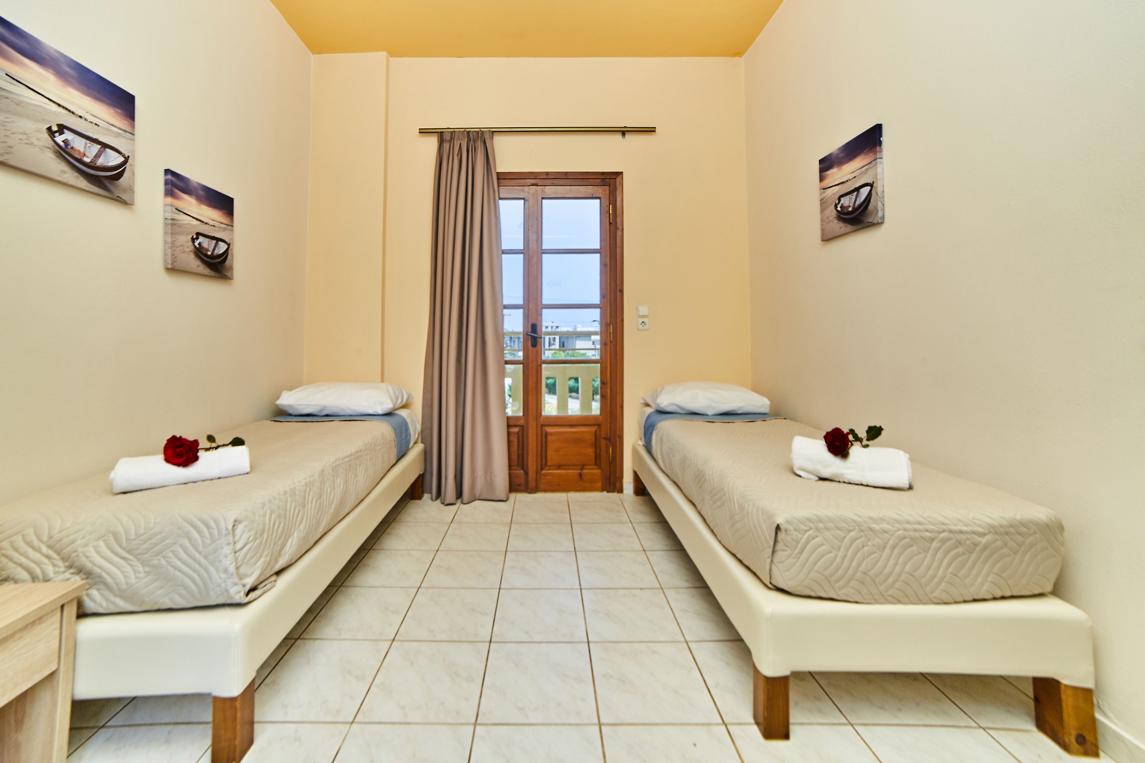 Habitación de hotel con dos camas individuales, una puerta de madera, una ventana con cortinas y obras de arte en las paredes.
