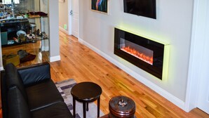A modern living room with a fireplace, wooden flooring, a black leather sofa, and a small round table. - Rio Vista Suites (Santa Cruz)