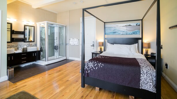 A modern bedroom with a four-poster bed, a walk-in shower, and a large mirror. - Rio Vista Suites (Santa Cruz)