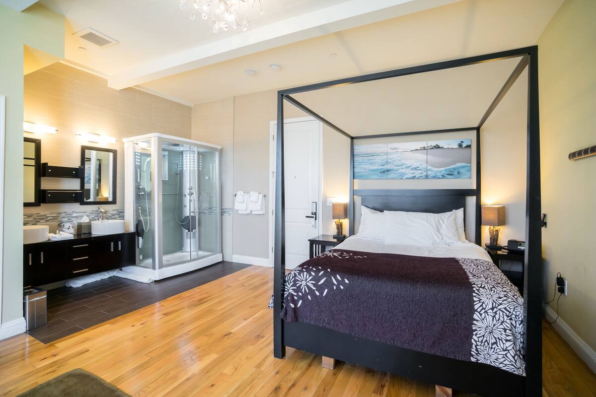 A modern bedroom with a four-poster bed, a walk-in shower, and a large mirror.