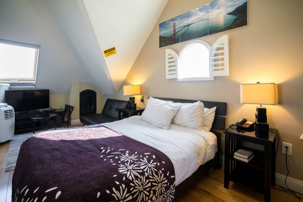 A bedroom with a bed, bedside lamps, a TV, and a painting of a bridge.