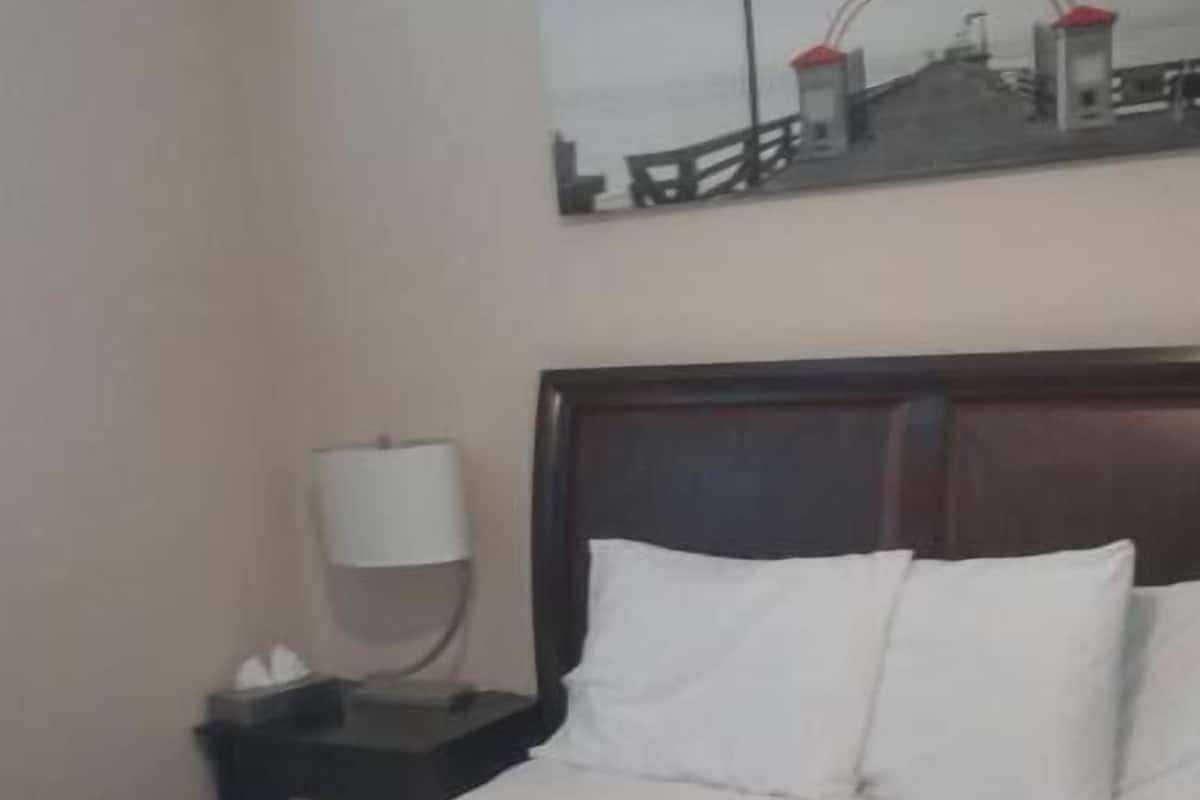 A hotel room with a bed, a nightstand, a lamp, and a painting on the wall.