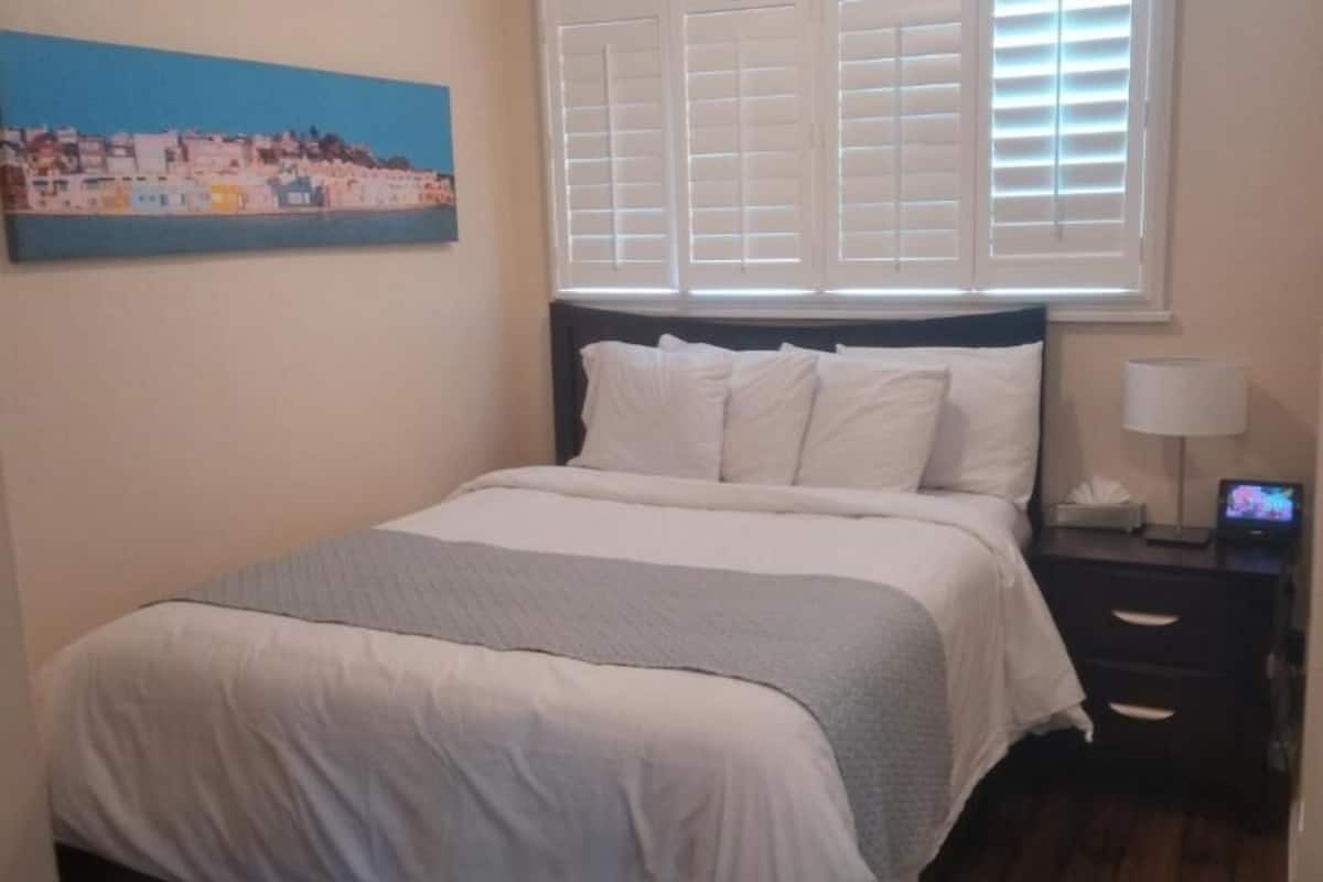 A neatly made bed with white bedding, a nightstand with a lamp, and a painting on the wall.