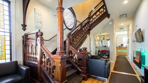 A grand staircase with intricate woodwork, leading to a second floor. A cozy seating area with a sofa and armchairs is visible on the first floor. - Rio Vista Suites (Santa Cruz)