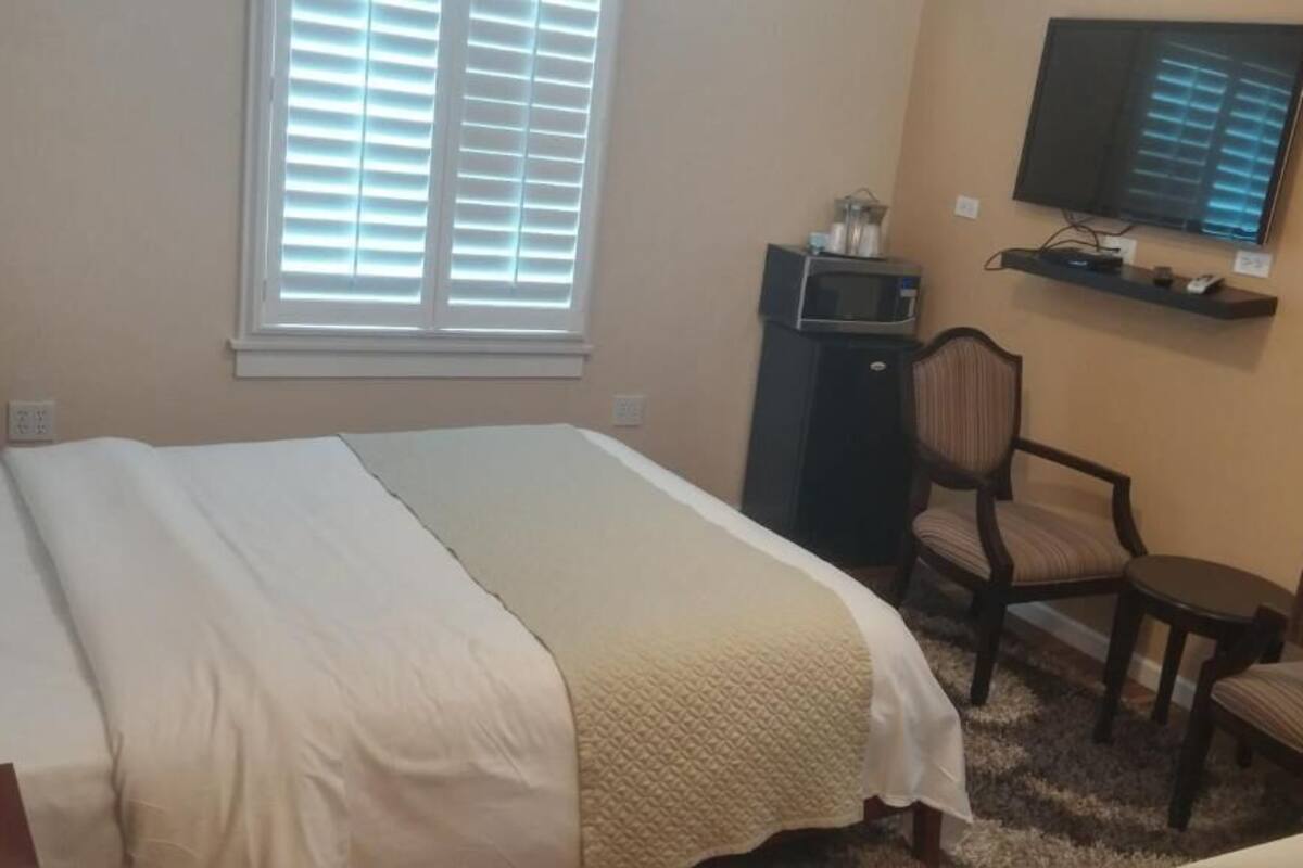 A hotel room with a bed, a TV mounted on the wall, a microwave, and a chair.