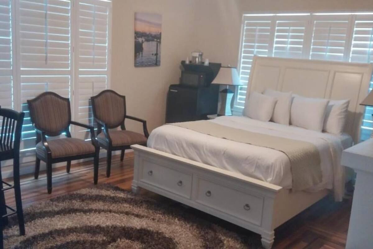 A bedroom with a bed, two chairs, a desk, and a lamp.