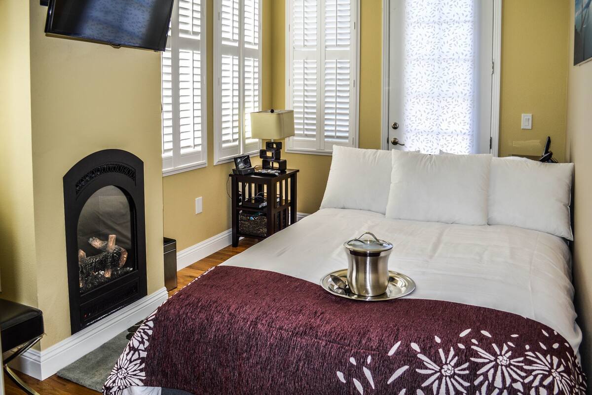 A hotel room with a bed, a fireplace, a TV, and a window with shutters.