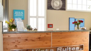 A reception desk with a sign reading "Rio Vista Suites." There is a clock on the wall and a window with blinds. - Rio Vista Suites (Santa Cruz)