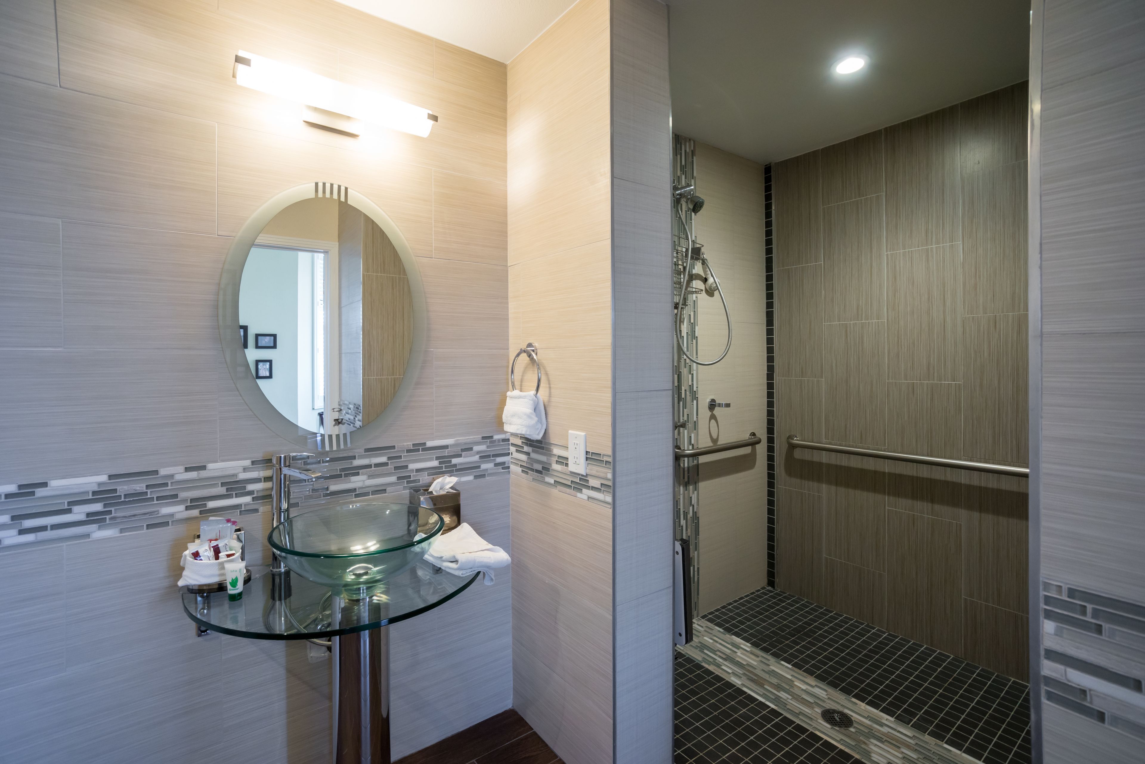 A modern bathroom with a glass sink, a round mirror, and a shower area.