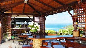 An outdoor bar area with wooden furniture, a view of the ocean, and a wooden ceiling structure. - Spring Hotel Bequia (Bequia Island)