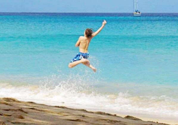 A person jumping into the sea with a boat in the background.