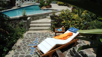 A pool area with a lounge chair, a wooden bridge, and a stone-tiled deck.