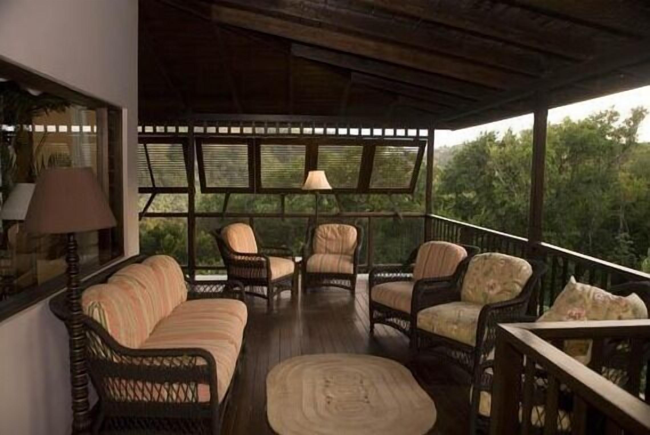 A covered outdoor seating area with wicker furniture and a view of the surrounding greenery.