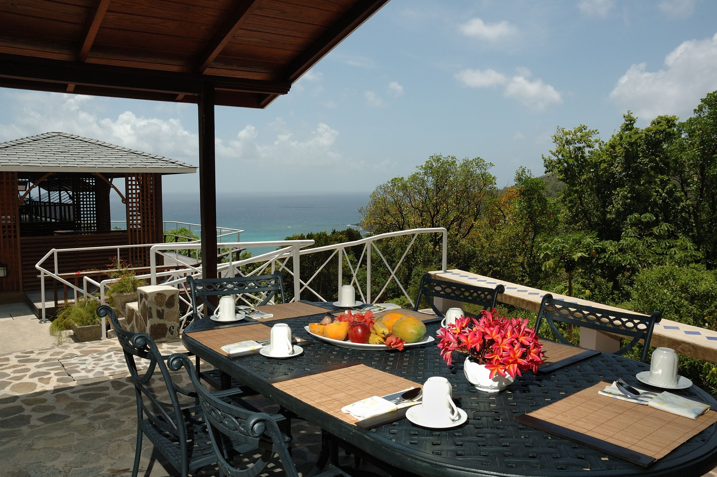 Un área de comedor al aire libre con una mesa preparada para dos, con vistas a un paisaje marino.