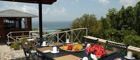 Un área de comedor al aire libre con una mesa preparada para dos, con vistas a un paisaje marino.