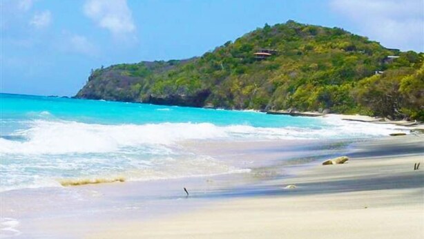 A beach with clear turquoise water, a sandy shore, and a hill with vegetation and a structure on top. - Spring Hotel Bequia (Bequia Island)