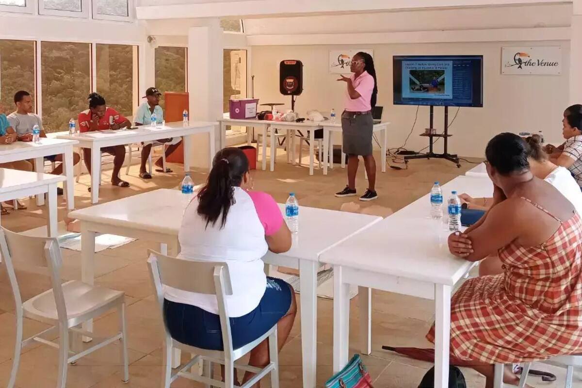 A conference room with white tables and chairs, a presentation screen, and a speaker.