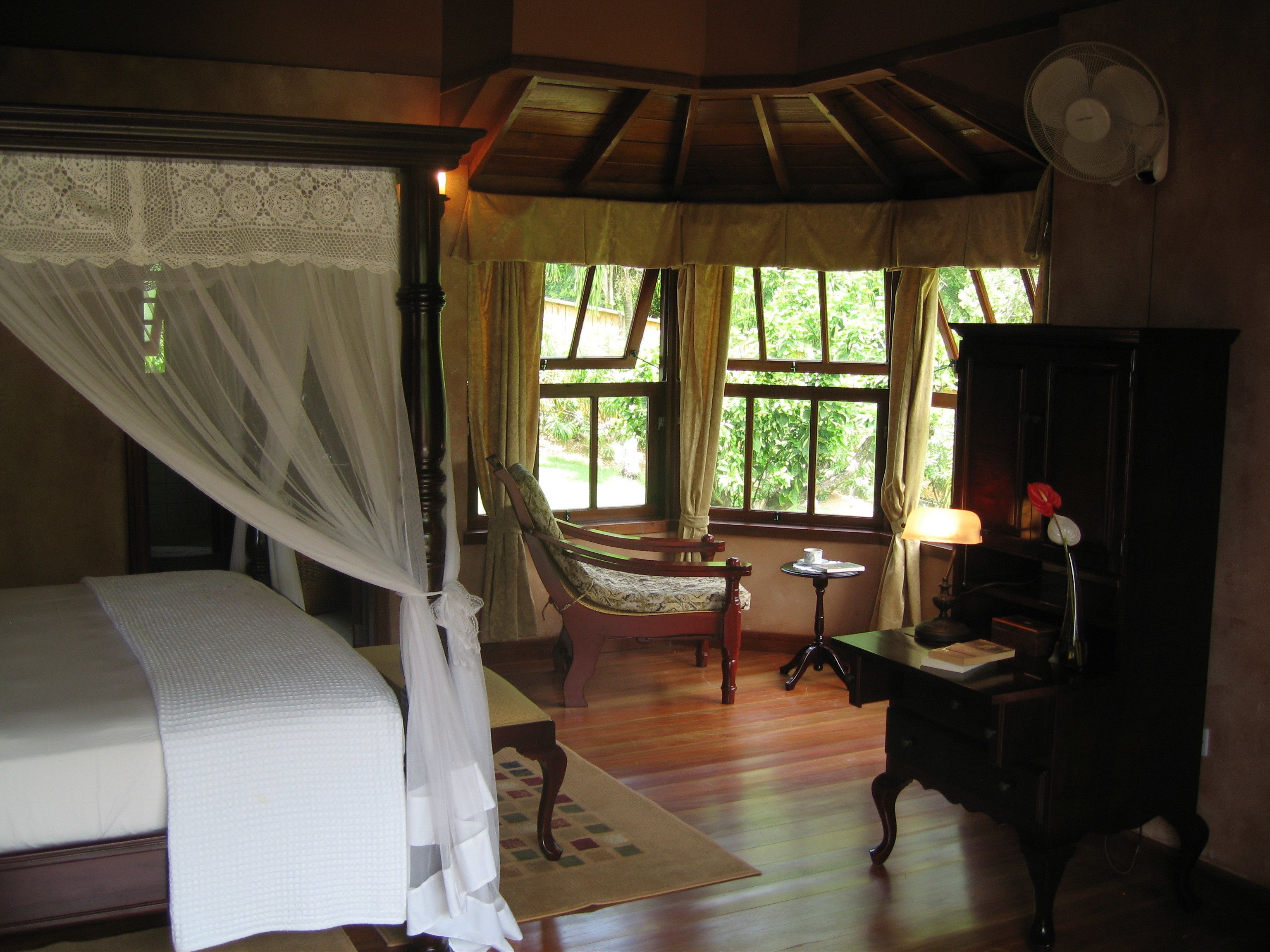 A bedroom with a four-poster bed, a chair, a small table, and a cabinet.