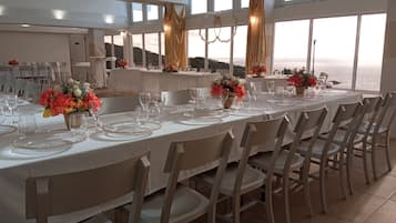 Uma longa mesa de jantar posta com toalhas brancas, pratos com detalhes dourados e centros de mesa florais.