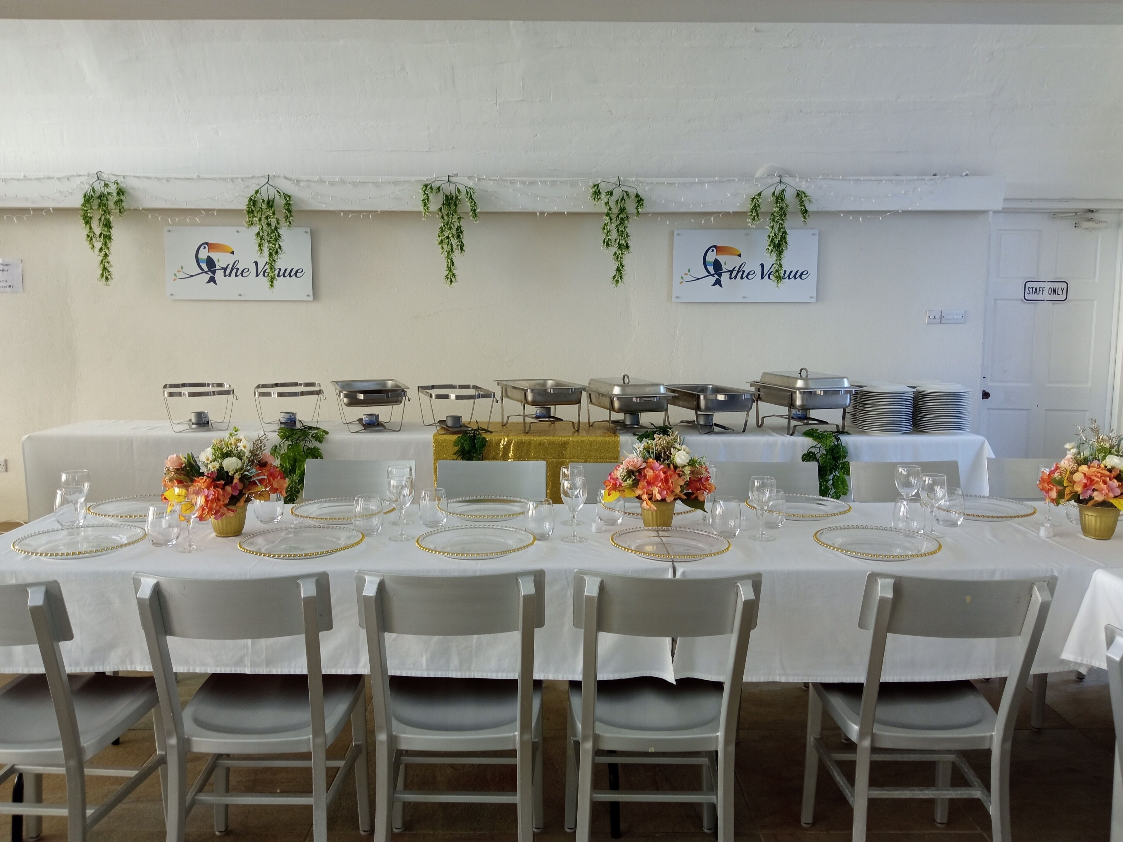 A banquet hall with tables set for a formal event, featuring white tablecloths, gold-rimmed plates, and floral centerpieces.