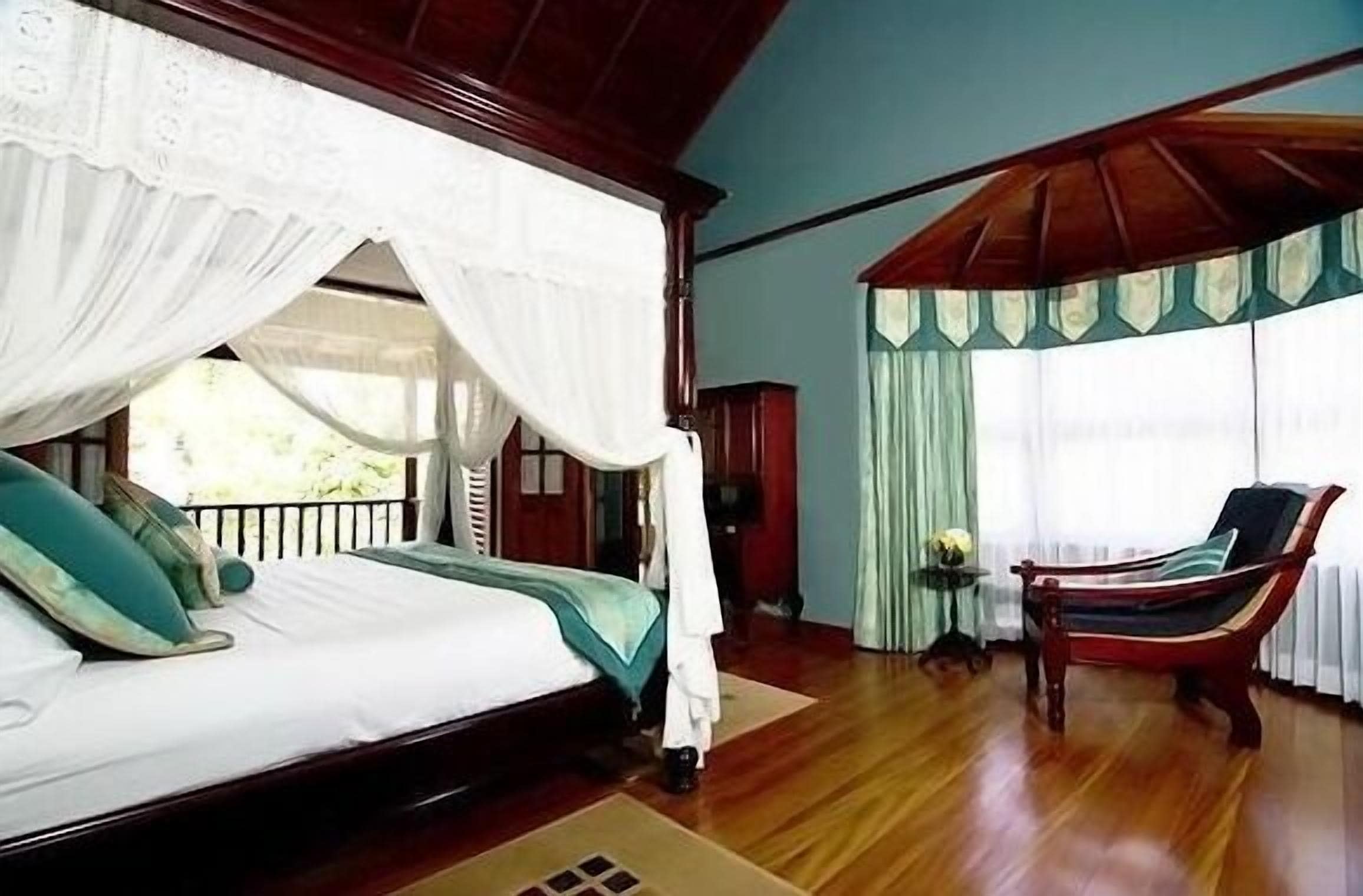 A bedroom with a four-poster bed, a wooden floor, a daybed, and a view of the outdoors.