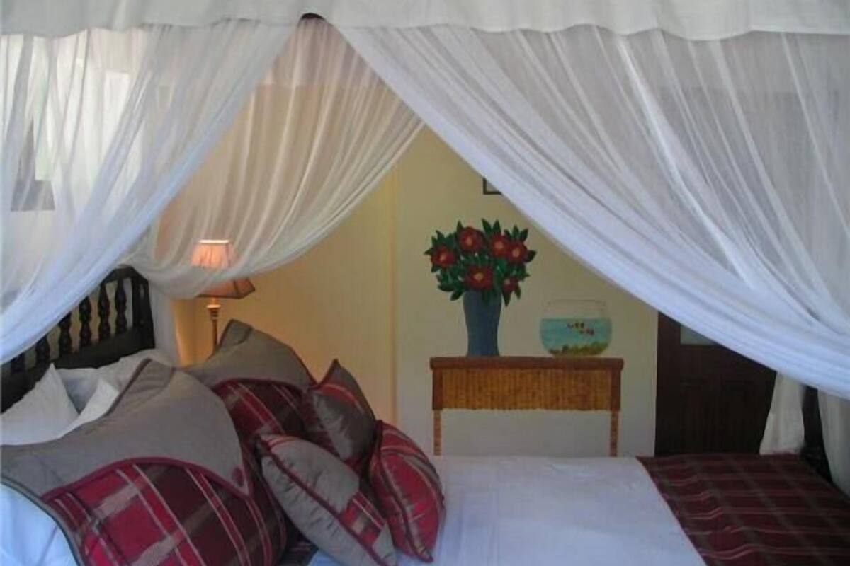 A bed with a canopy, pillows, a bedside table with a vase of flowers, and a fishbowl.