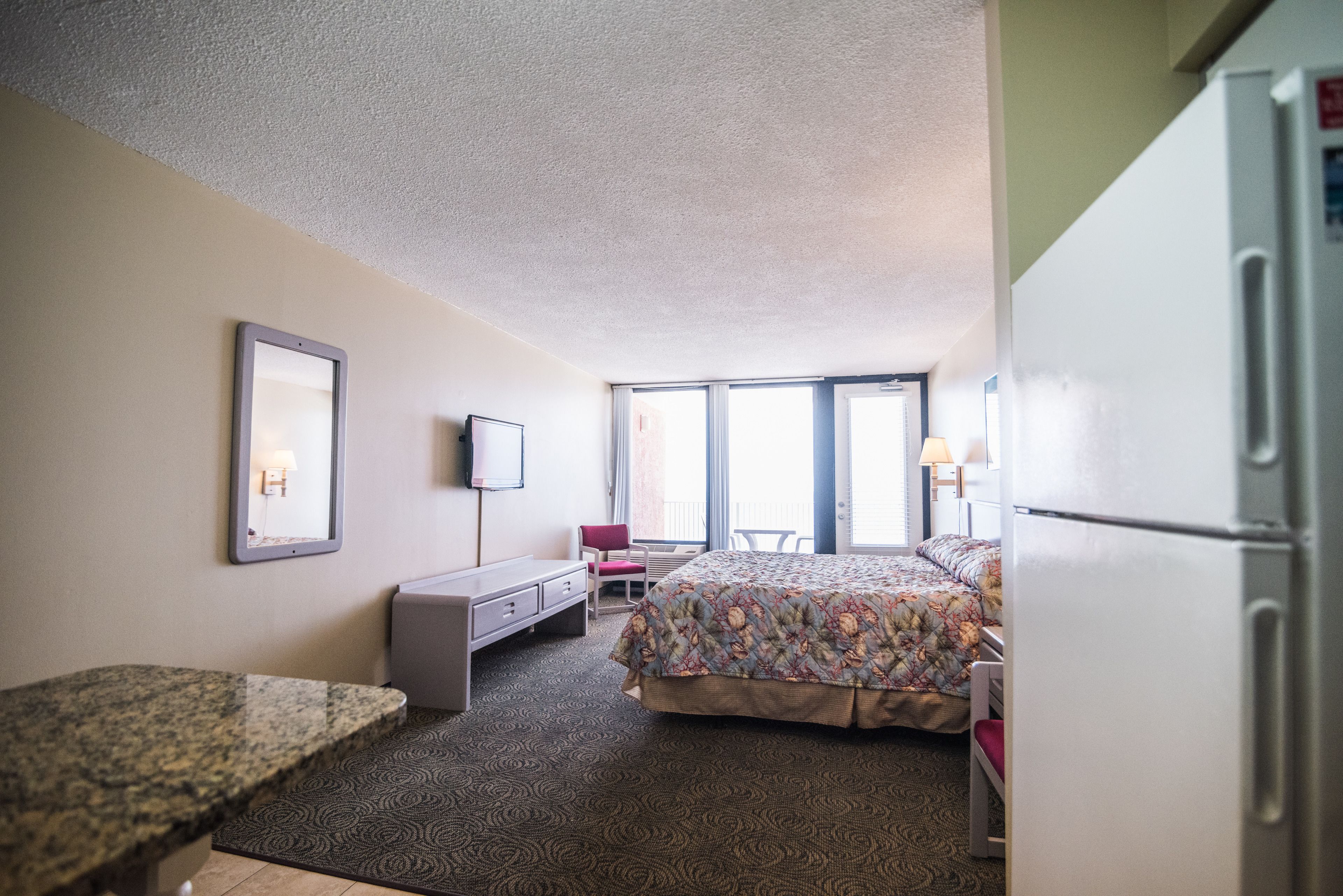 A hotel room with a bed, a desk, a chair, a television, and a refrigerator.