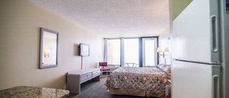 Una habitación de hotel con cama, escritorio, silla, televisión y refrigerador.