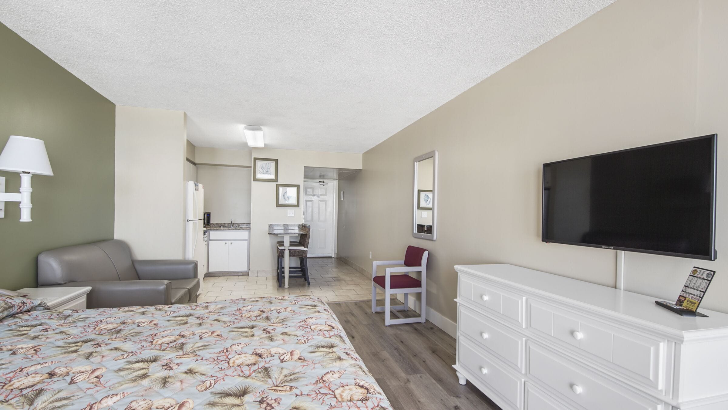 A hotel room with a bed, a desk, a chair, a television, and a dresser.