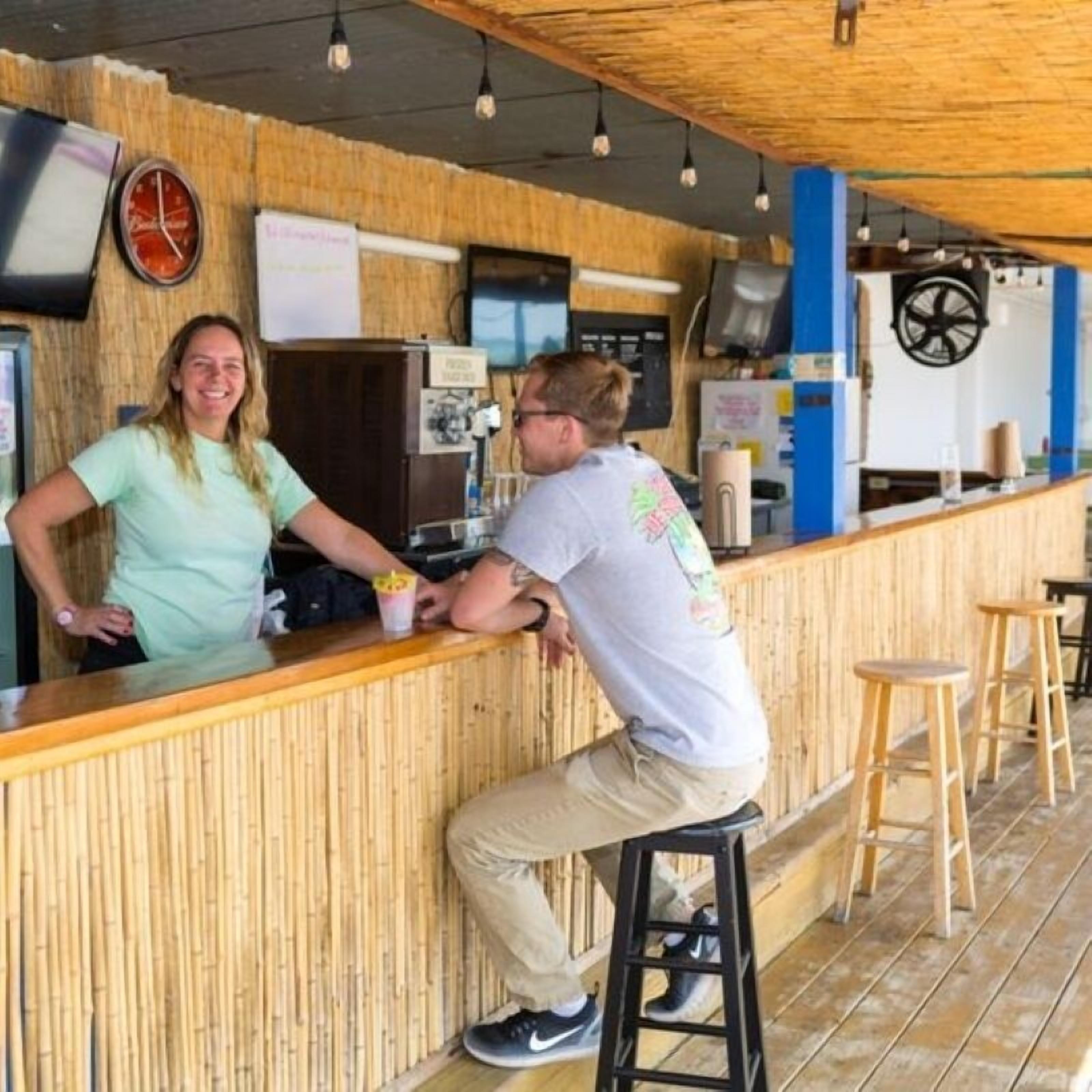 Een bar met een houten toonbank, krukken, een klok en een tv aan de muur.