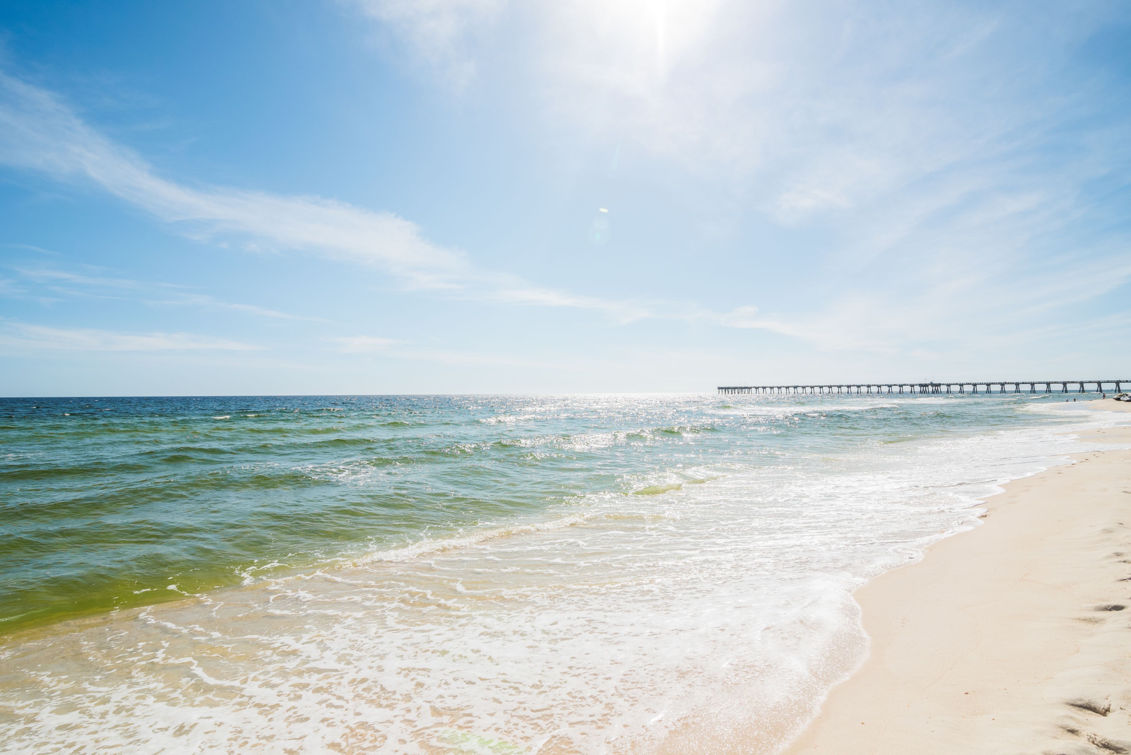 A beach with clear skies, a pier extending into the water, and gentle waves.
