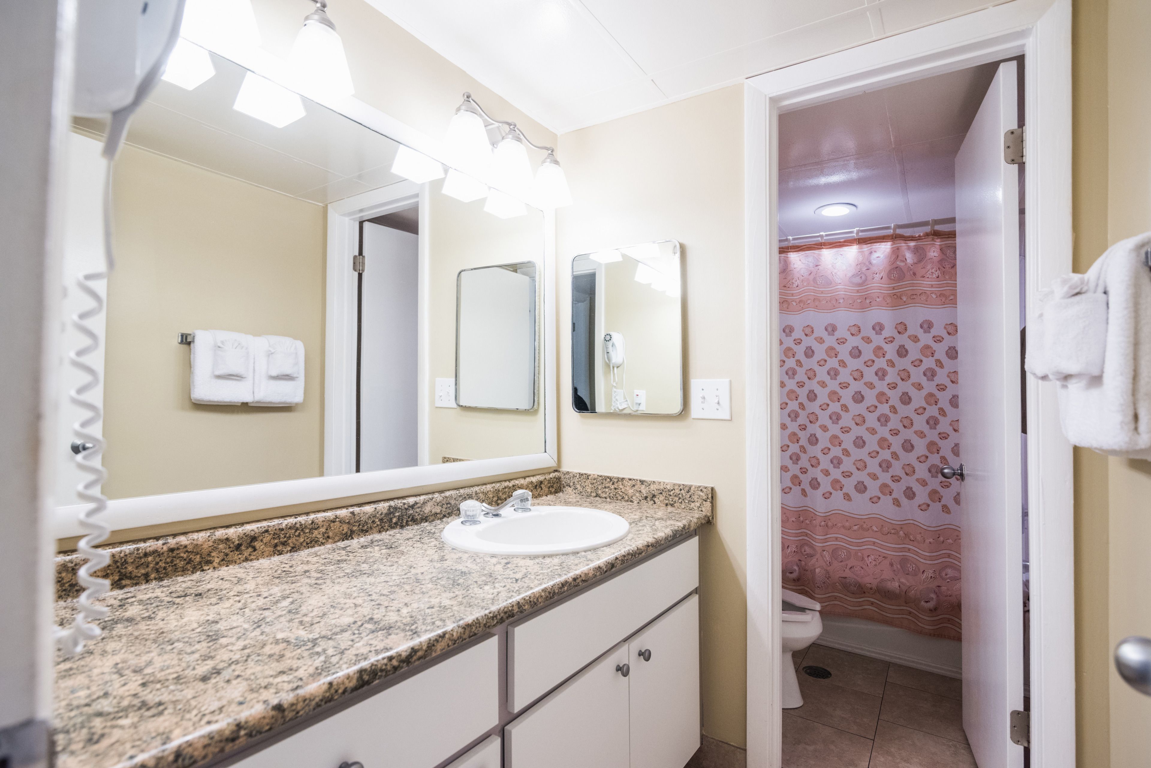 Un bagno con lavabo su piano in granito, doppio specchio e tenda della doccia a motivi floreali.