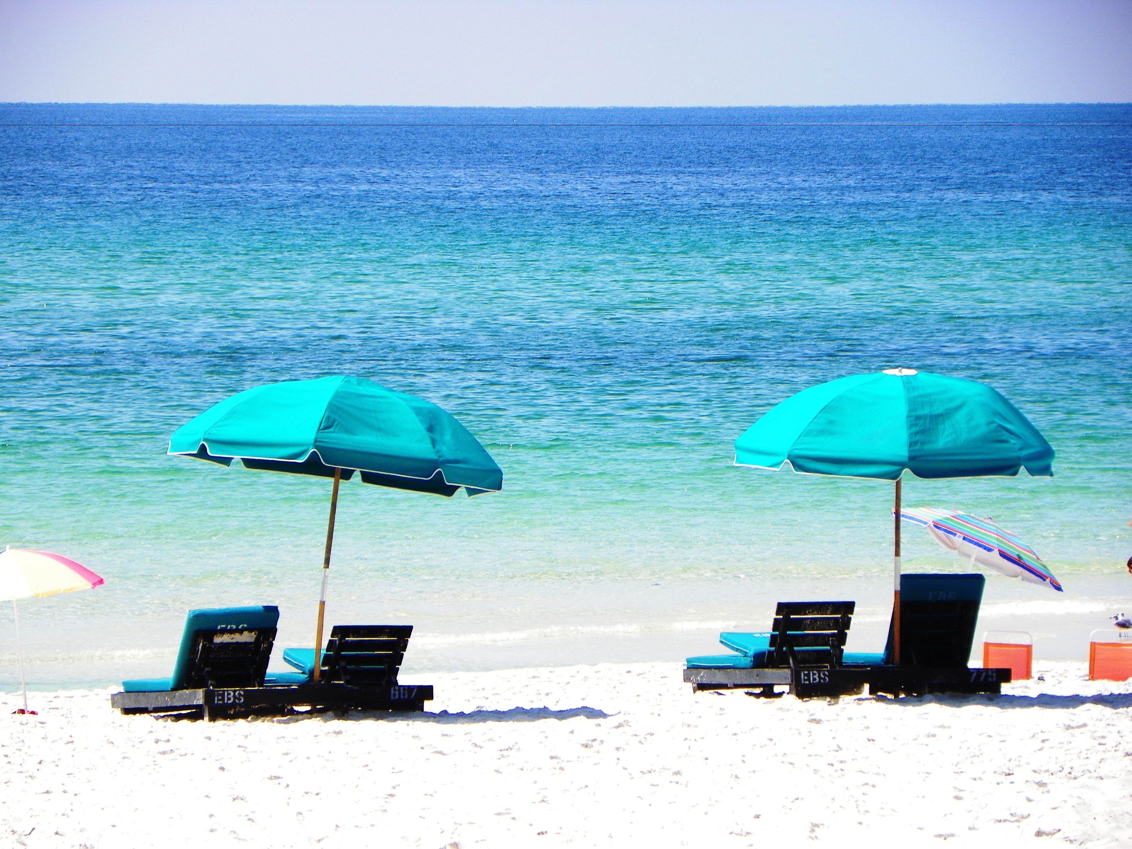 Two beach chairs with umbrellas and a beach chair with a striped umbrella.