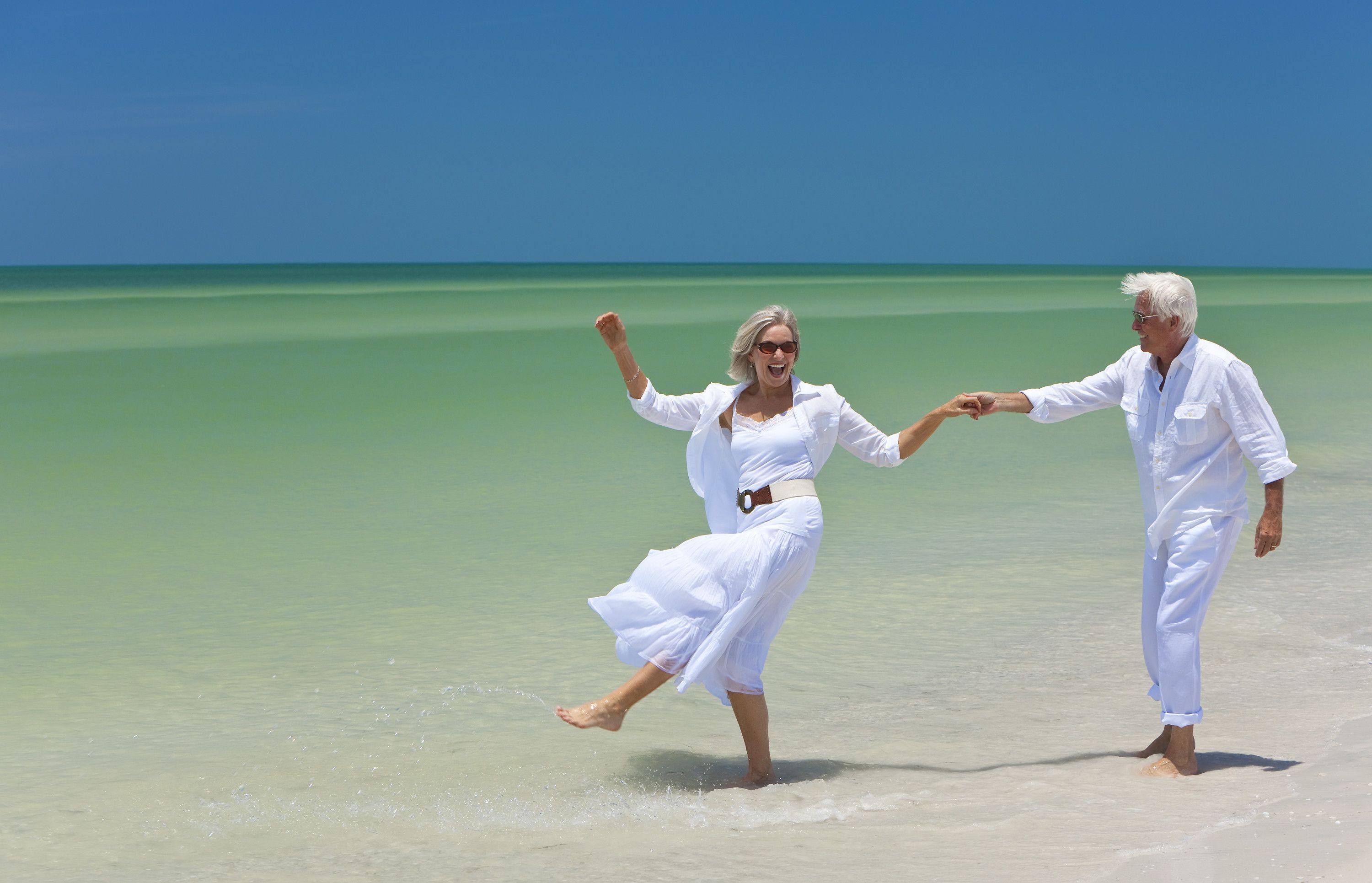 Un couple se tenant la main sur une plage, avec une eau cristalline et un ciel bleu.