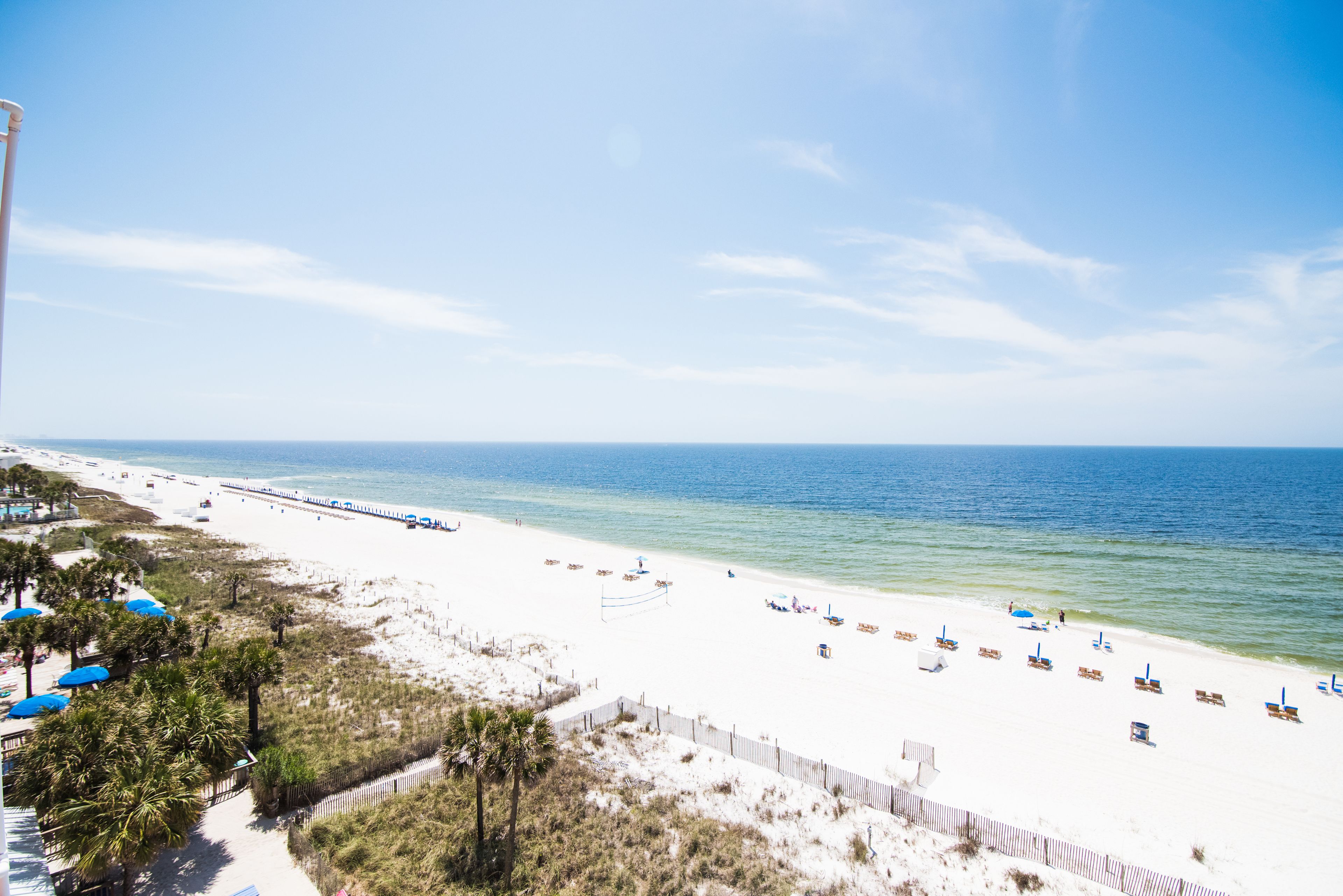 A beach with white sand, clear blue water, and a wooden pier extending into the sea.