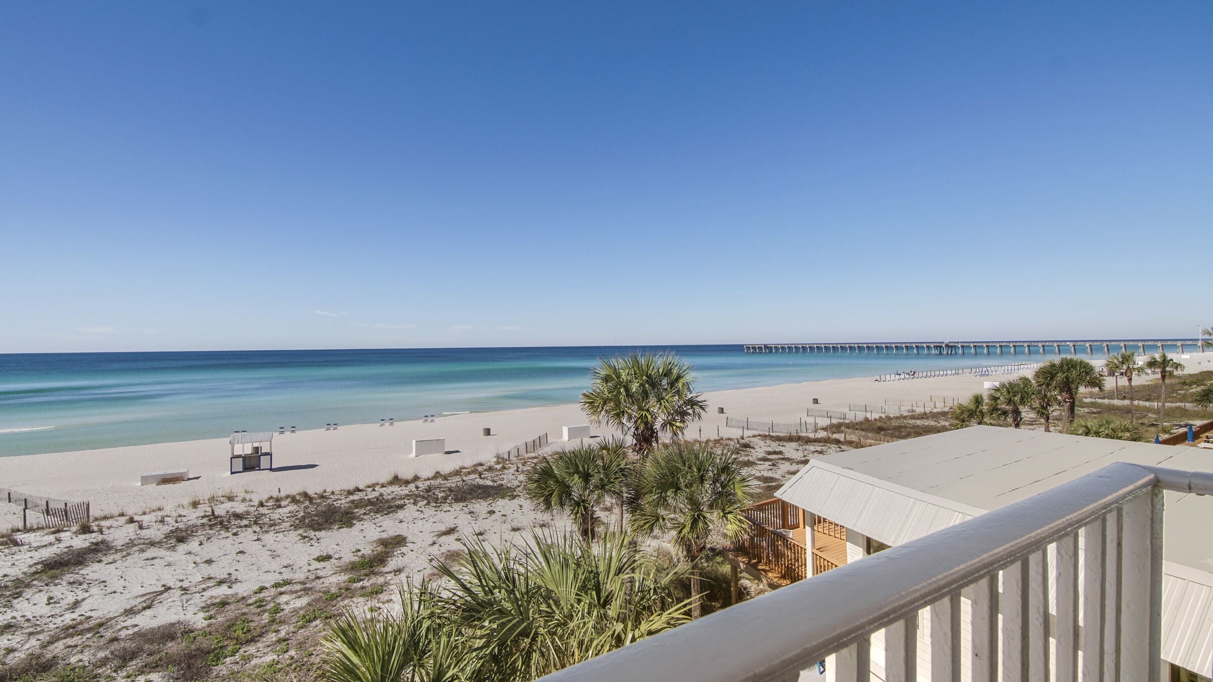 A beach view with a pier extending into the ocean, sandy beach, and palm trees.