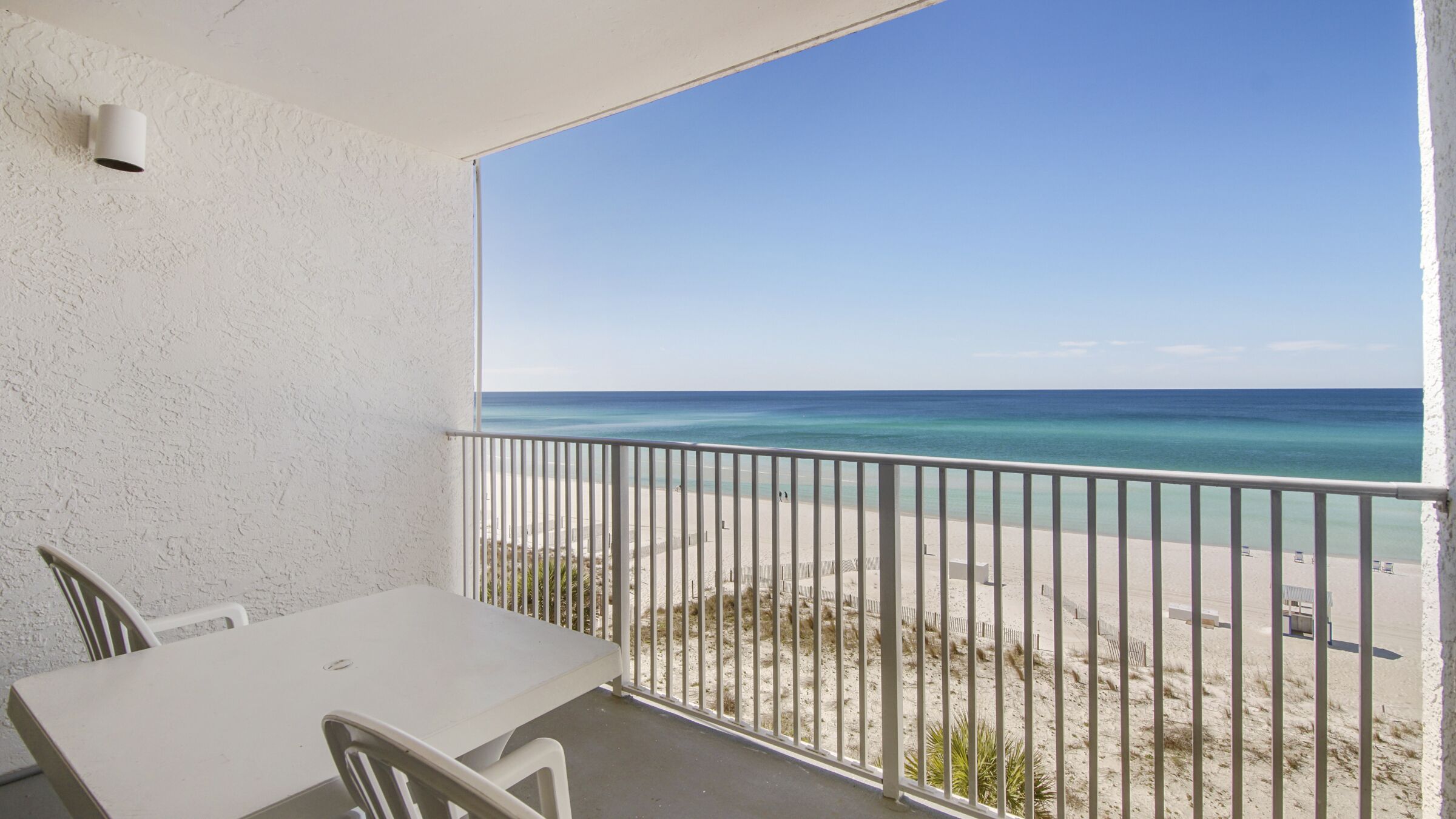 Un balcón con vista a la playa, una mesa y sillas.