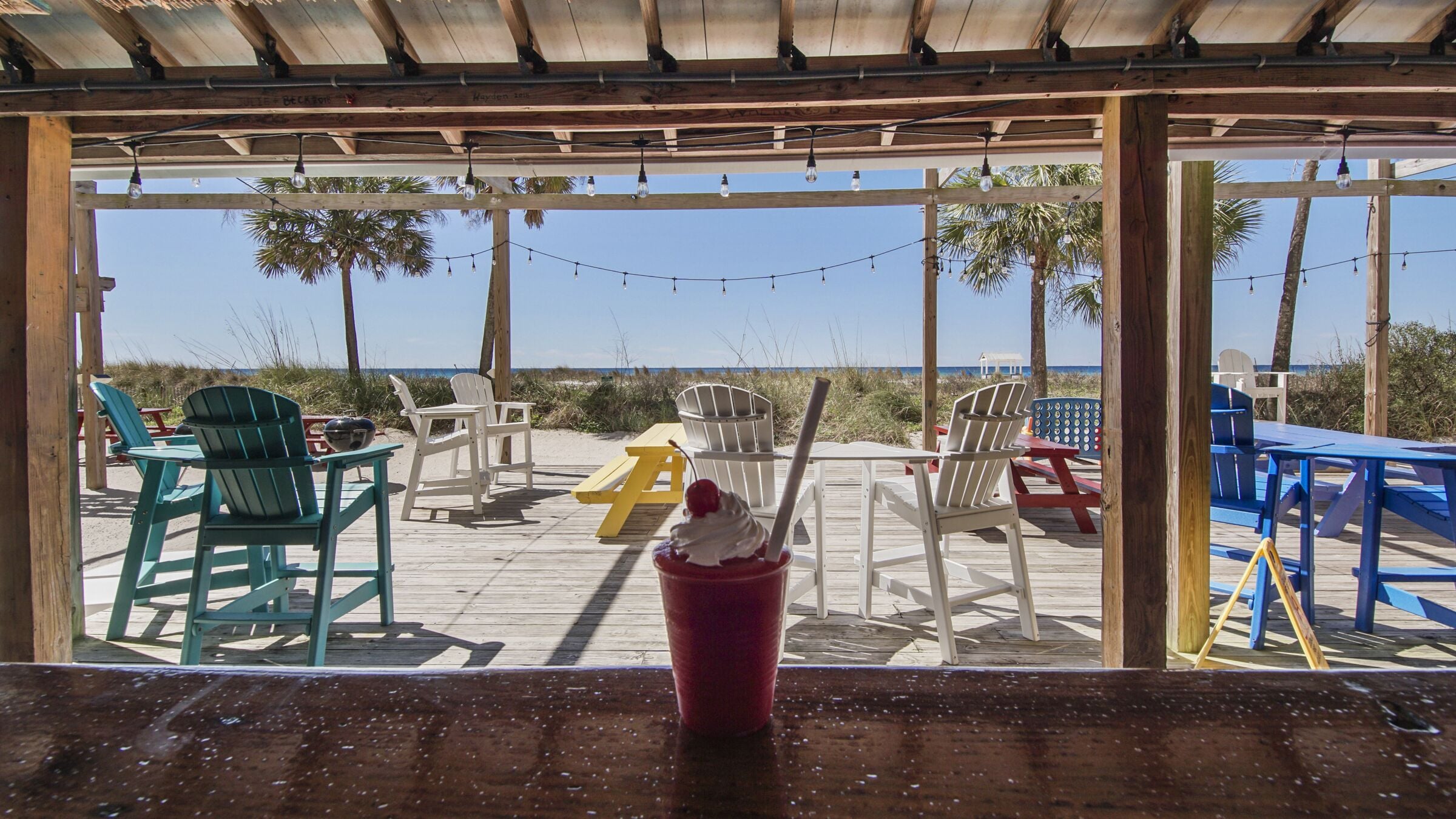 A beachside deck with wooden furniture and string lights.