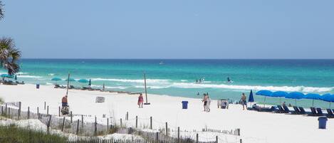 A beach with a wooden fence, beach umbrellas, and people.