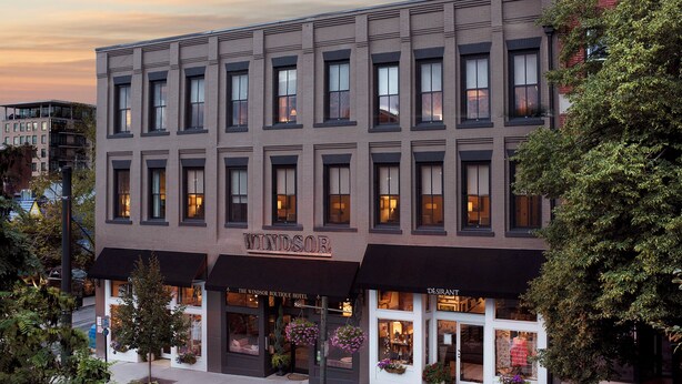 Un hotel de varios pisos con fachada moderna, grandes ventanales y un letrero que dice 'The Windsor Boutique Hotel'.