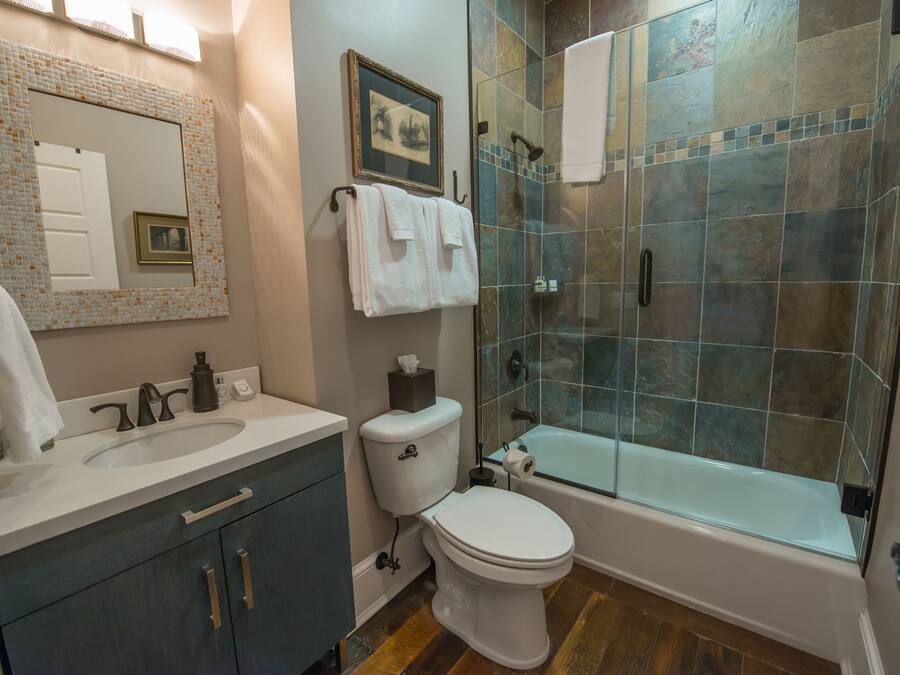 A modern bathroom with a large mirror, white sink, dark cabinets, a toilet, and a glass-enclosed shower area.